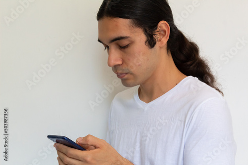 portrait of a non binary hispanic man with long hair on a white background using a cell phone