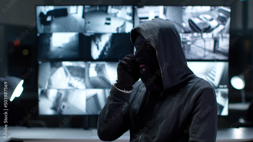 Criminal in mask sit in monitoring center with cctv footage and talking on phone Criminal in mask sit in monitoring center with cctv footage and talking on phone