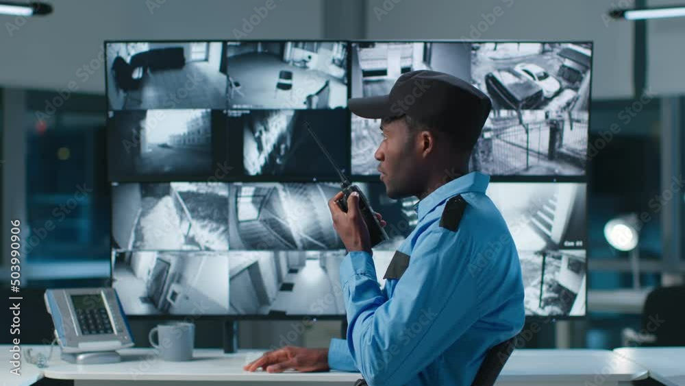 African-American security officer watching the screens talking on radio in control room 
