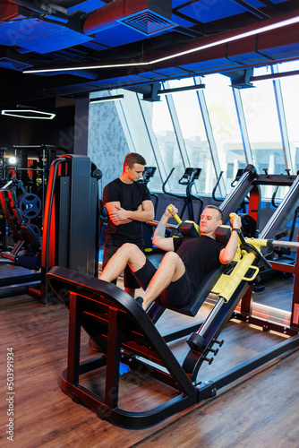 Athletic man doing exercises with the help of his personal trainer in a public gym.