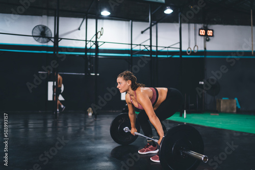Young female athlete with barbell equipment doing deadlift exercise in sportive gym studio, Caucaisan fit girl with strength power training and weightlifting for feeling vitality wellness photo