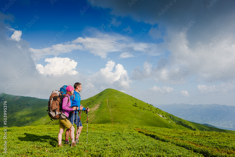 Young couple with backpacks hiking in the mountains and enjoying valley view