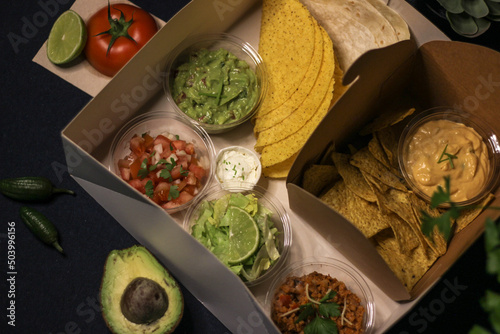 Mexican food box, tex mex, Taco, chili, tortilla, nachos chips, cheddar cheese, guacamole, sour cream, lettuce, tomato