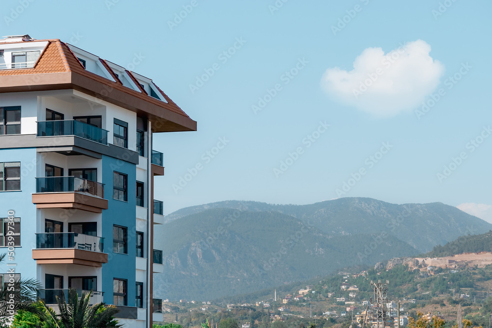 Part of an apartment building against the backdrop of a mountain and blue sky.