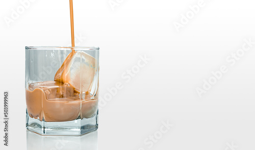 Licor de crema cayendo en copa de cristal transparente con hielos en su interior photo