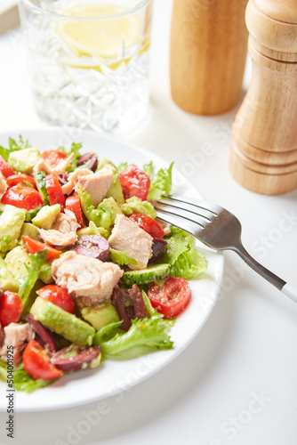 Salad with tuna, lettuce, cucumbers, tomatoes, olives and avocados in white plate on the table