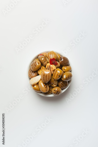 grilled green olives in oil, pitted, with red hot pepper and garlic in a white bowl on a light background, view from above