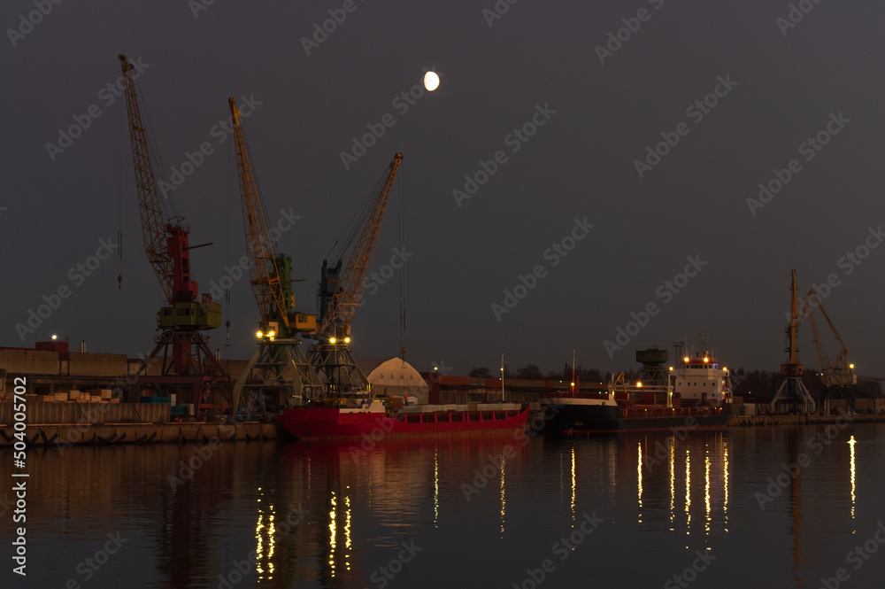 Three cranes in the port against clear evening sky. Moon shining in the sky
