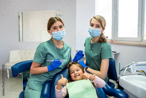 Pediatric female dentist with assistant with child girl patient  showing thumbs up