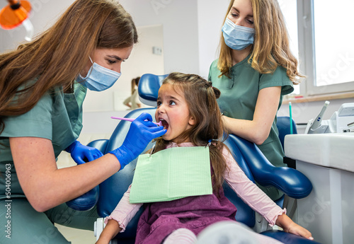 фотографія Beautiful female dentist with her assistant in medical uniform looking at children's teeth