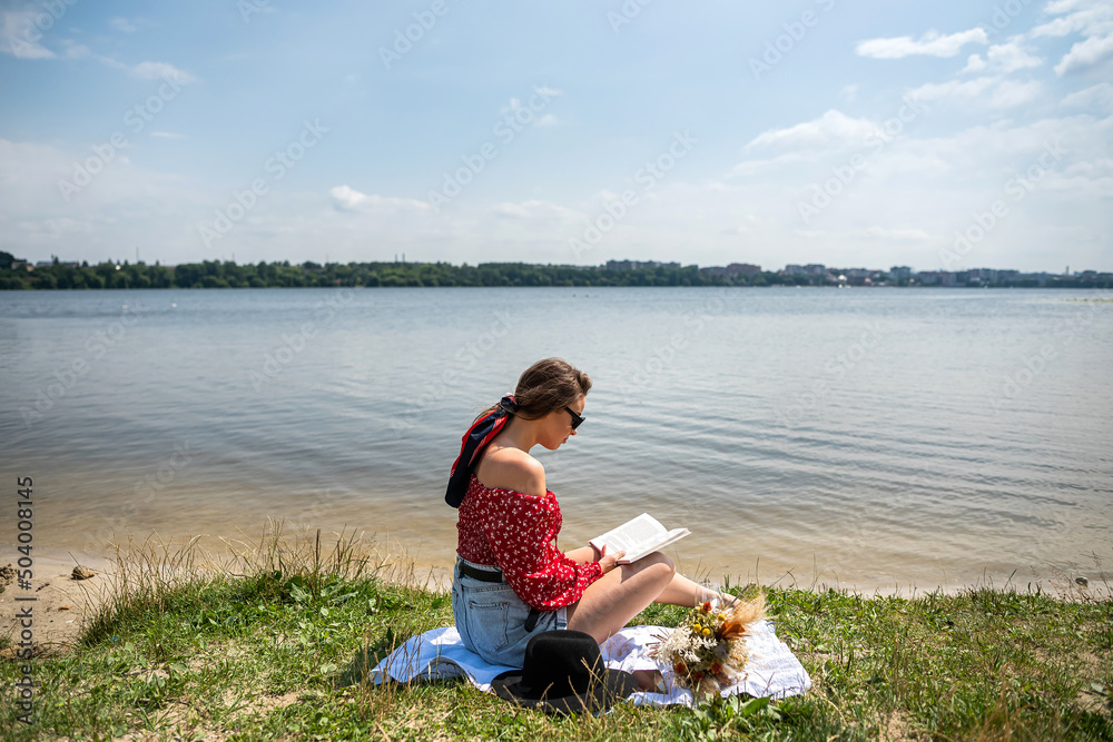 Beautiful woman read book sitting on grass near the lake.