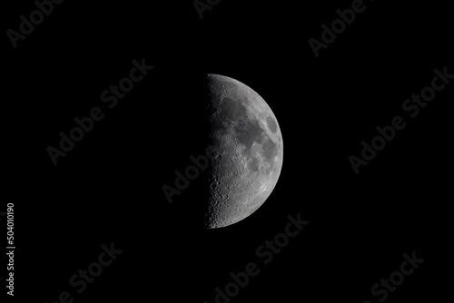 Black and white photograph of half of the large moon with craters and seas. Satellite of the Earth in the phase of the first quarter. Astronomy and astrophotography through a telescope.