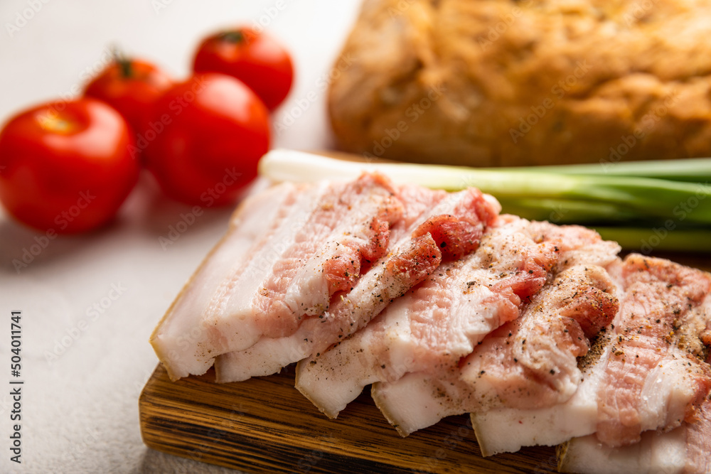 Board with pork fat, green onions, homemade bread and cherry tomatoes on a gray stone background. Salo. Delicious salty lard with pepper. Space for copy. Space for text.