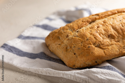 Fresh homemade bread on a kitchen towel on a gray cement background. Bread with flax seeds, sunflower seeds and sourdough bran. Organic homemade baked goods. Place to copy.