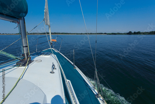White yacht on the river bank in the calm. Folded sails in windless sunny weather. Sea travel. Yachting. © INTHEBLVCK