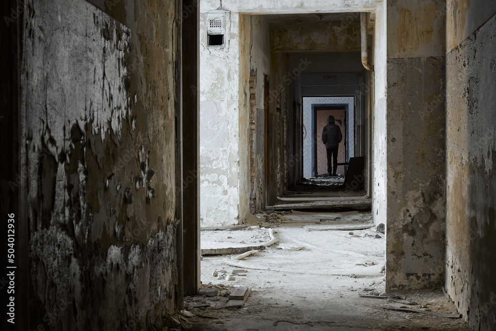 Man stands in abandoned corridor. Rear view of man standing in corridor at abandoned building