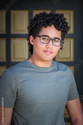 A young man with curly hair posing in front of a green door with beige square panels.