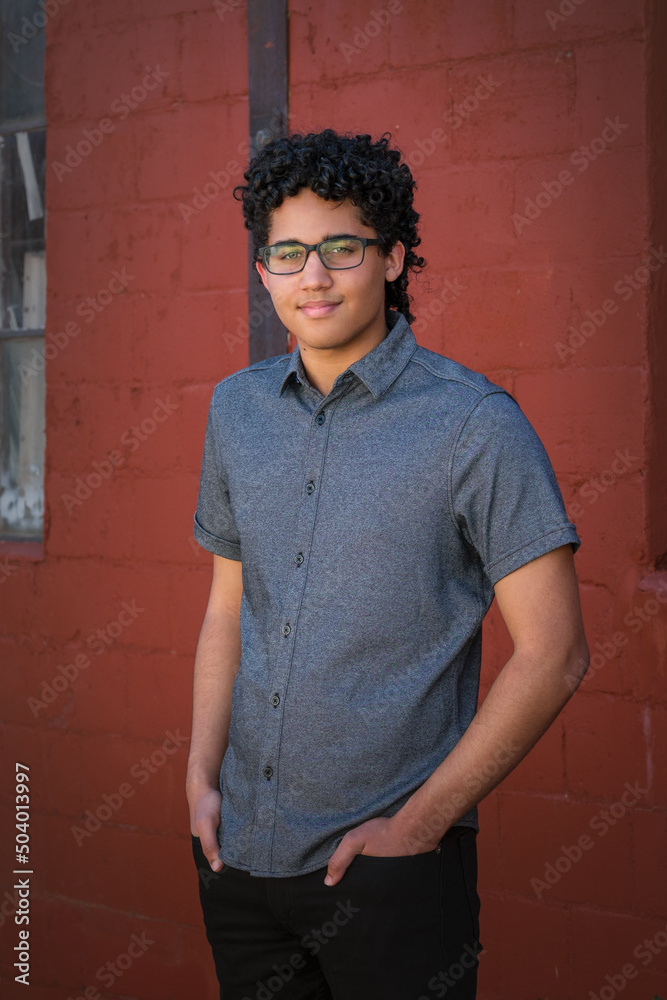 Obraz premium A young man stands in front of a red brick wall with his hands in his pockets.