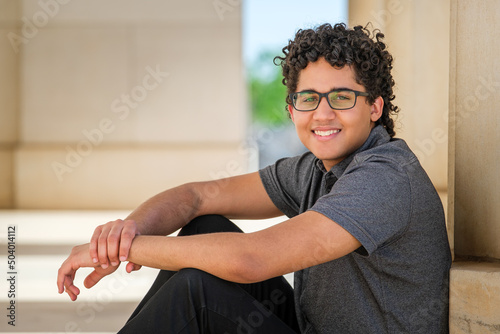 a curly-haired young man sits and leans against a stone pillar