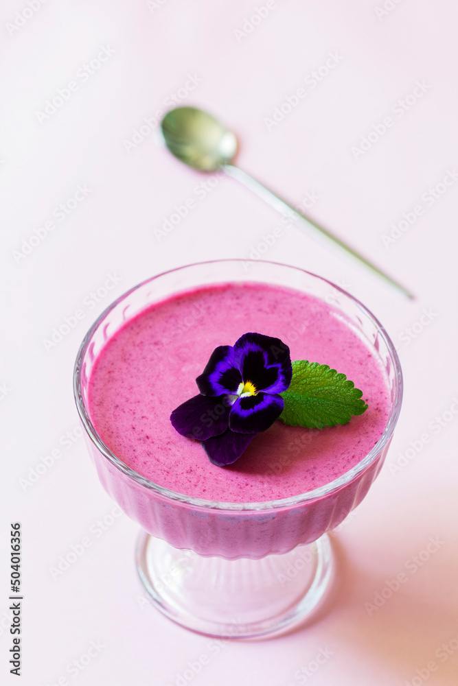 Blackcurrant berry mousse garnished with viola flower and lemon balm leaf.