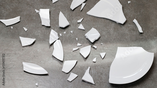 Closeup of broken dishes and white shards on the gray floor tiles background, splinters of break plate. Fragments tableware in kitchen. Shard, pieces of shattered dish ceramic. top view