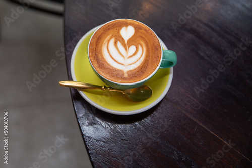 green mug of cappuccino with latte art on wooden background.