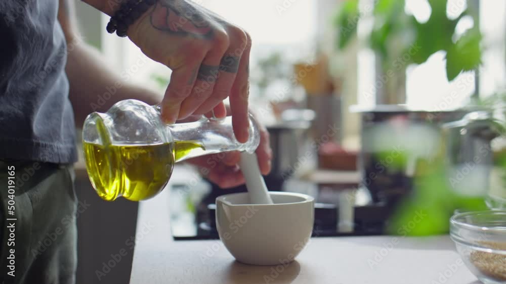Cropped shot of unrecognizable chef pouring olive oil into mortar and using pestle while preparing paste