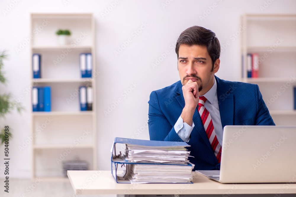 Young male employee unhappy with excessive work in the office Young male employee unhappy with excessive work in the office