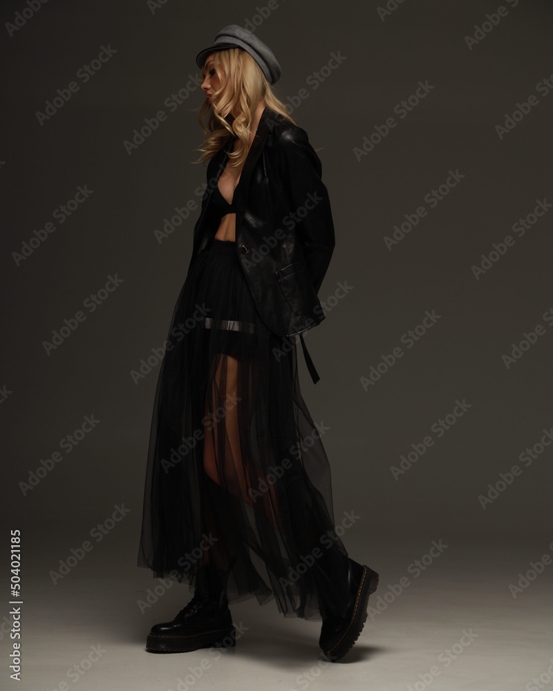 Fashionable american blonde pretty woman in black eco leather boots, jacket, transparent tulle skirt, studio shoot