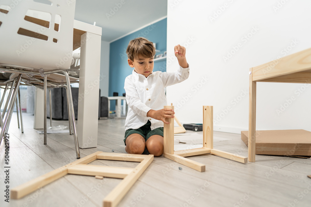 Small caucasian boy four years old playing with self assembly chair or table on the floor at home in day - little child assembling furniture alone childhood craft concept front view copy space Small caucasian boy four years old playing with self assembly chair or table on the floor at home in day - little child assembling furniture alone childhood craft concept front view copy space