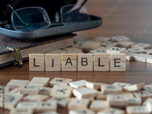 liable word or concept represented by wooden letter tiles on a wooden table with glasses and a book photo