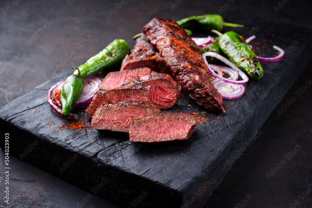 Traditional barbecue sirloin steak with chili and onion rings served as close-up on a charred wooden board