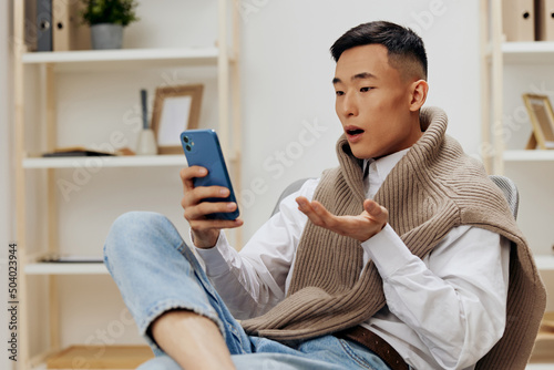 teenager communication with the phone in his hands sits on a chair interior
