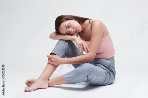 Despondent young brunette woman feeling sad sitting on floor and leaning on knee against isolated background © Mediaphotos