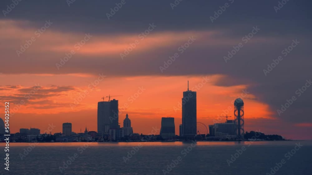 Time laps sunset sea and sunset against background of resort town. Batumi in Georgia. City is located on seafront in red sunset of sun clouds. journey. silhouette of city at sunset in clouds. ocean Time laps sunset sea and sunset against background of resort town. Batumi in Georgia. City is located on seafront in red sunset of sun clouds. journey. silhouette of city at sunset in clouds. ocean