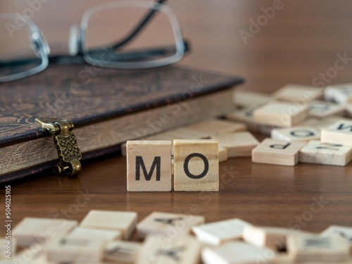 the acronym mo for modus operandi word or concept represented by wooden letter tiles on a wooden table with glasses and a book photo