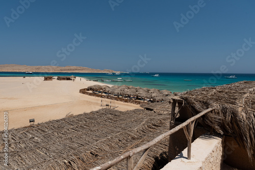 Holidays in Egypt. Beach with umbrellas made of dry palm leaves, desert and yachts in the blue water of the Red Sea. Vacation and Holidays in Egypt. © PhotoRK