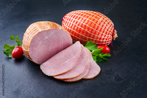 Traditional German boiled Easter ham with tomatoes and parsley offered as close-up on a black board with copy space