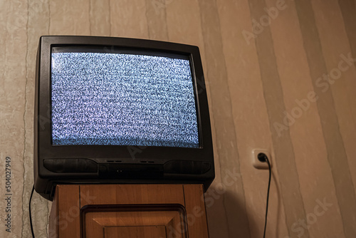 Retro old tube television with static glitch displayed on screen standing on wooden nightstand at hotel room or home