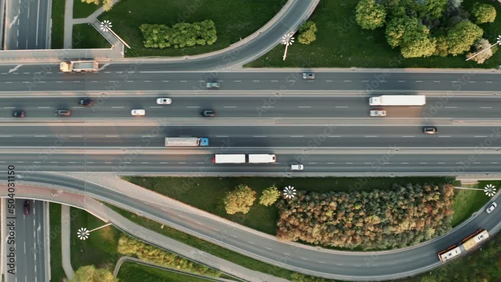 Aerial following shot elevated multiple roads junction. Drone footage city highway road junctions on sunny evening. Intersection freeway road overpass. Follow car. Summer day, green trees grass