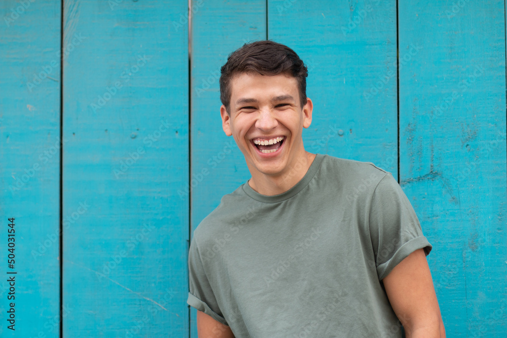 Obraz premium Young latin with an authentic laugh, in the background a blue door typical of latin homes. Latin representation in a portrait.
