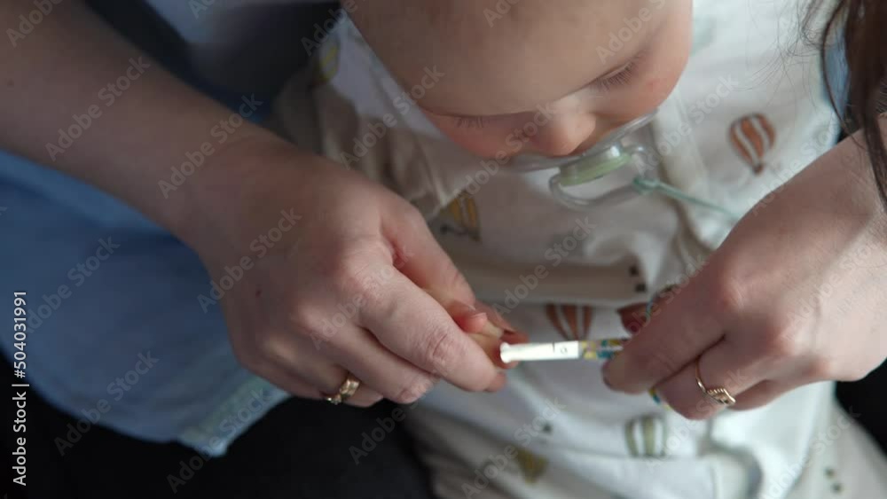 Mother trimming baby nails. Toddler infant on mom lap cutting clipping son nail. 