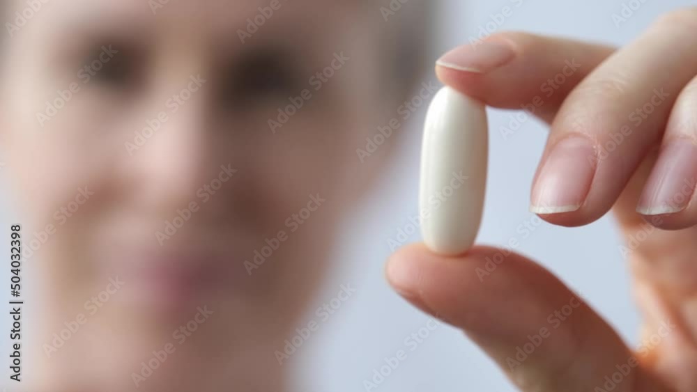 A woman holds a large white pill in her hand and examines it carefully. The hand with the pill is in the foreground in focus A woman holds a large white pill in her hand and examines it carefully. The hand with the pill is in the foreground in focus