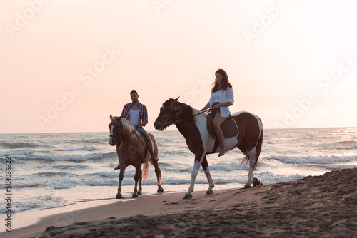 Fototapeta Naklejka Na Ścianę i Meble -  a loving couple in summer clothes riding a horse on a sandy beach at sunset. Sea and sunset in the background. Selective focus 