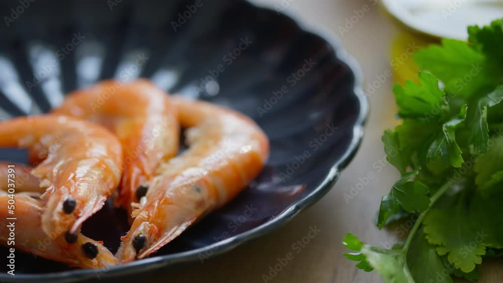 Close up tracking shot of hand of male chef putting freshly cooked shrimps on plate next to bunch of green parsley Close up tracking shot of hand of male chef putting freshly cooked shrimps on plate next to bunch of green parsley