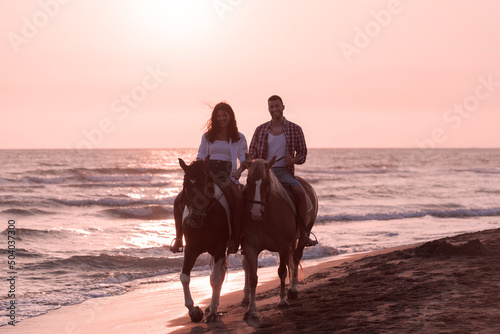a loving couple in summer clothes riding a horse on a sandy beach at sunset. Sea and sunset in the background. Selective focus 