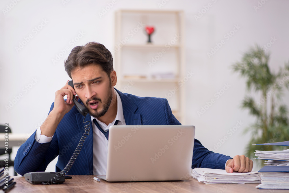 Young male employee unhappy with excessive work in the office Young male employee unhappy with excessive work in the office