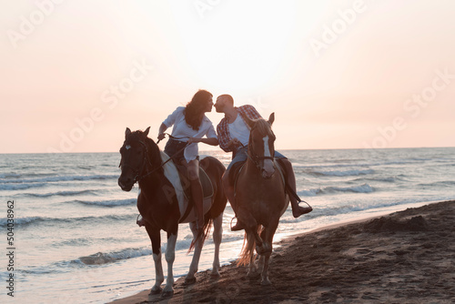 a loving couple in summer clothes riding a horse on a sandy beach at sunset. Sea and sunset in the background. Selective focus 
