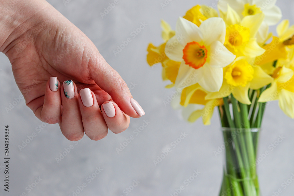 Spring or summer neat nude manicure with floral ornament against blurred flowers. Fashion and beauty. Close-up