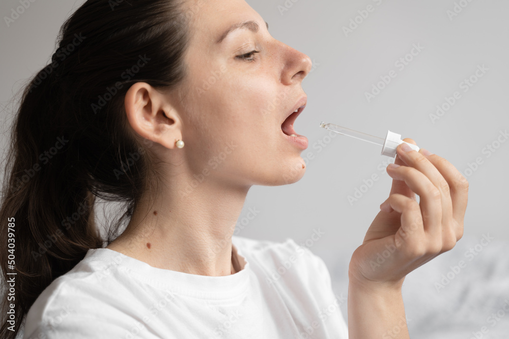 Portrait of dark haired young woman taking oil supplement with glass dropper. CBD hemp medicine oil applying on the tongue Portrait of dark haired young woman taking oil supplement with glass dropper. CBD hemp medicine oil applying on the tongue